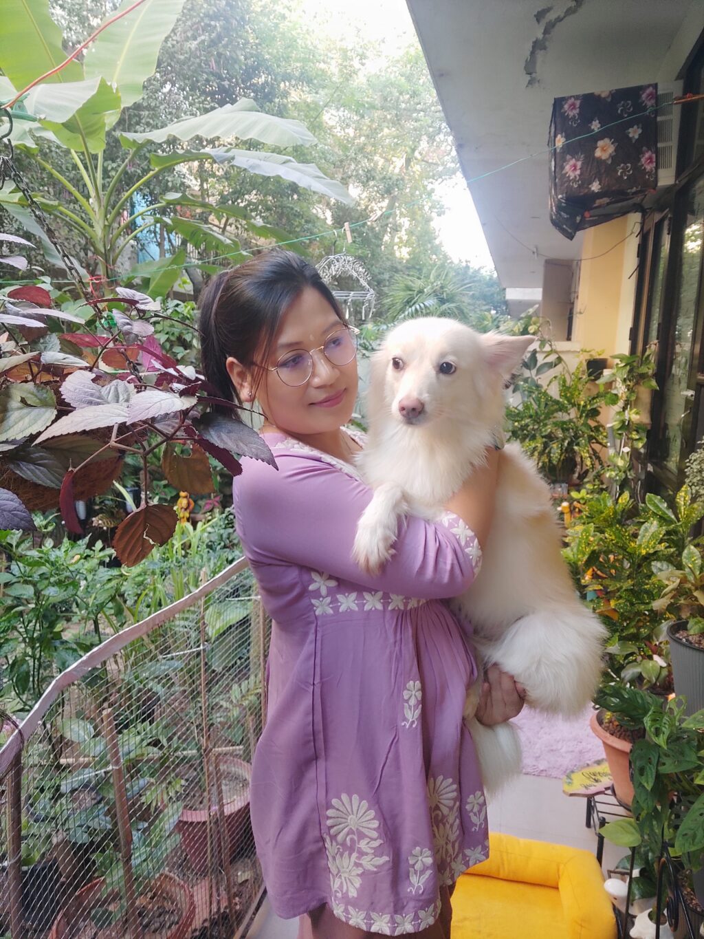 Nongmaithem Rita with her eldest female dog, Thoibi, in their home garden surrounded by plants and greenery.